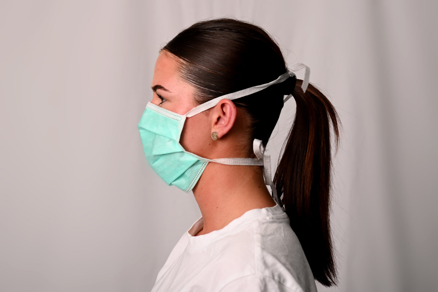 Person wearing a surgical face mask against a plain background