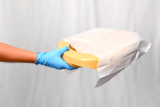 Hand wearing a blue glove holding a bedpan with bedpan cover against a white background