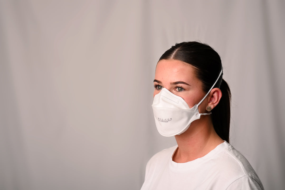 Person wearing a white P2 mask against a plain background
