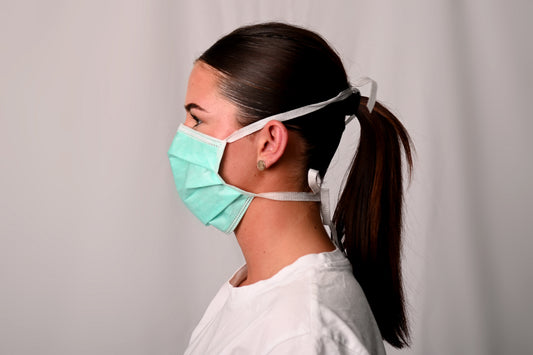 Person wearing a surgical face mask against a plain background