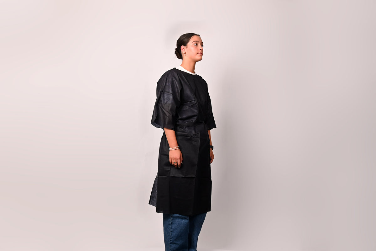 Person wearing a dark blue patient gown over a dark outfit on a light background
