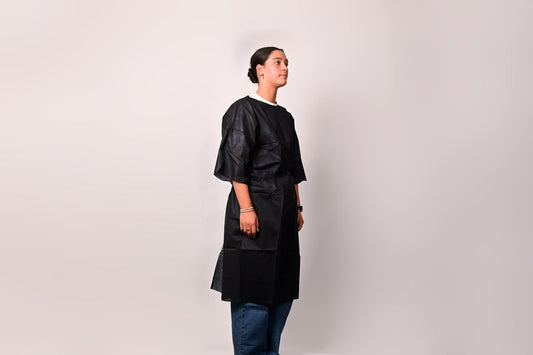 Person wearing a dark blue patient gown over a dark outfit on a light background