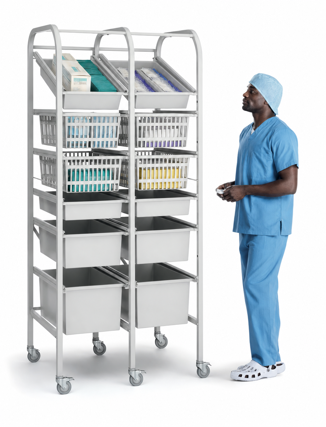 A tall silver medical supply cart with multiple bins and trays stands next to a person wearing blue scrubs and a matching cap on a white background.