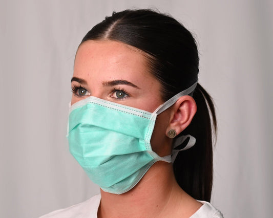 Woman wearing a green surgical mask against a plain background